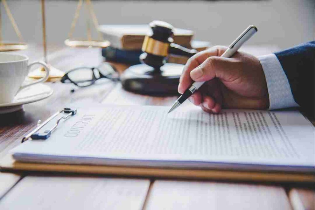 Hand signing a contract with a gavel, glasses, and a coffee cup in the background.
