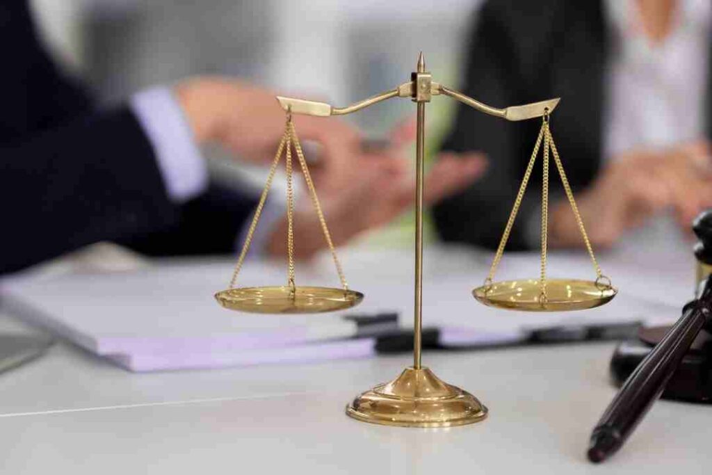 Close-up of scales of justice with people talking in the background.